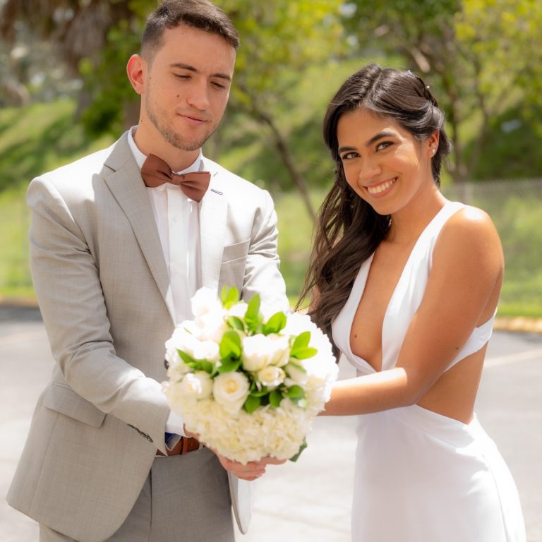 Bride and groom from Miami holding bouquet outdoors A groom in Miami and his brides holds a bouquet of flowers, smiling outdoors.