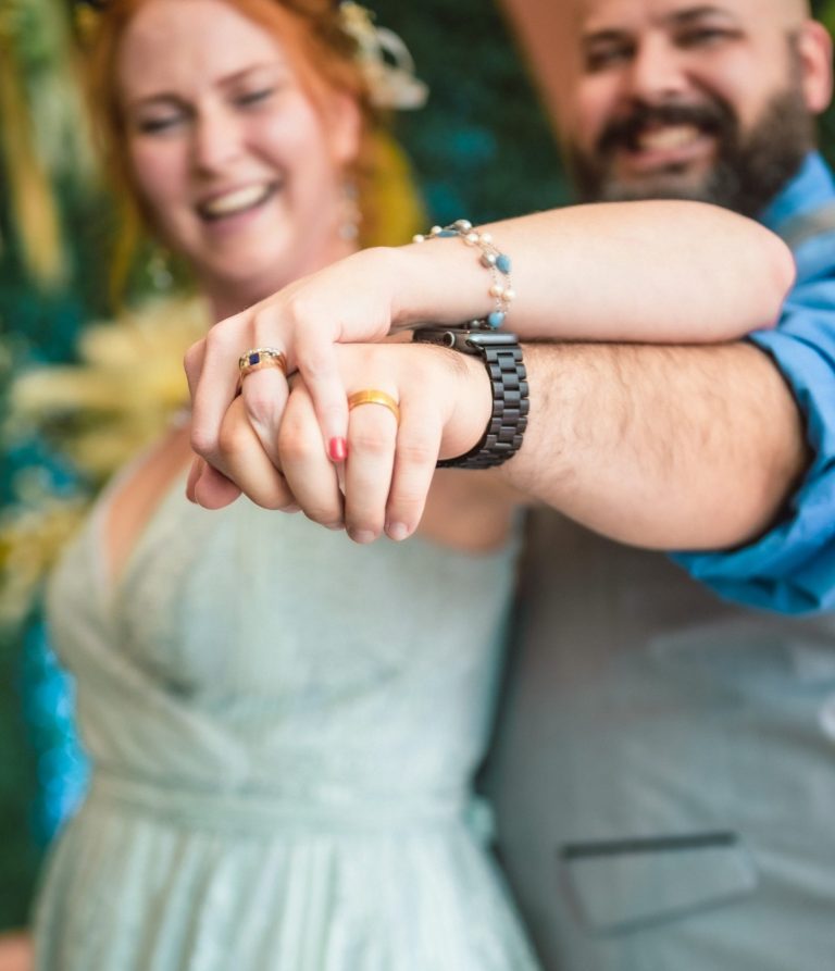 Couple showing off rings at Port of Miami by Iris Ramil Wedding Officiant A couple joyfully holding hands, smiling at the camera against a colorful backdrop by Iris Ramil Wedding Officiant.